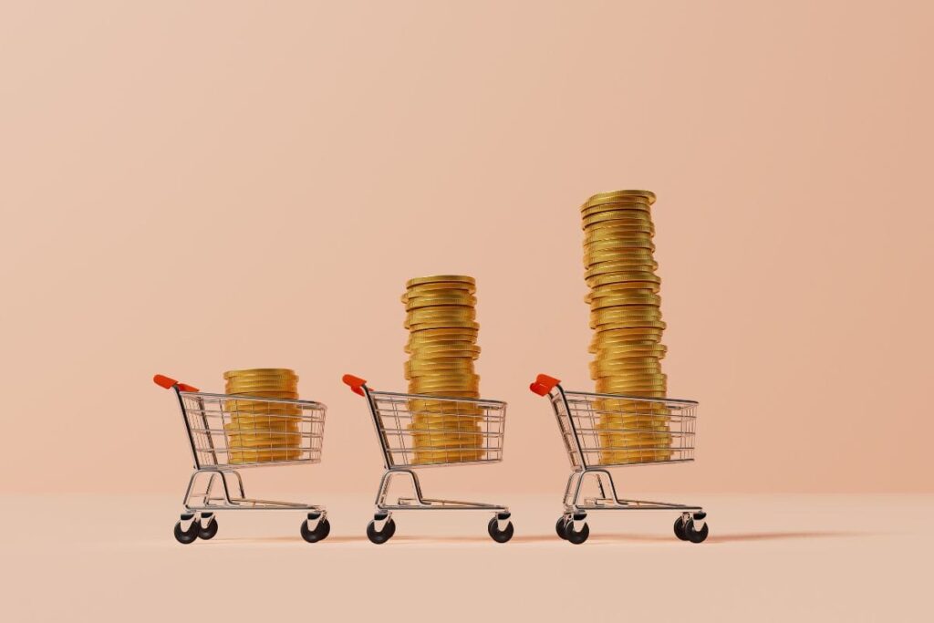 Três carrinhos de compras em fila contendo pilhas crescentes de moedas douradas, representando o aumento dos custos e o impacto da inflação no poder de compra ao longo do tempo